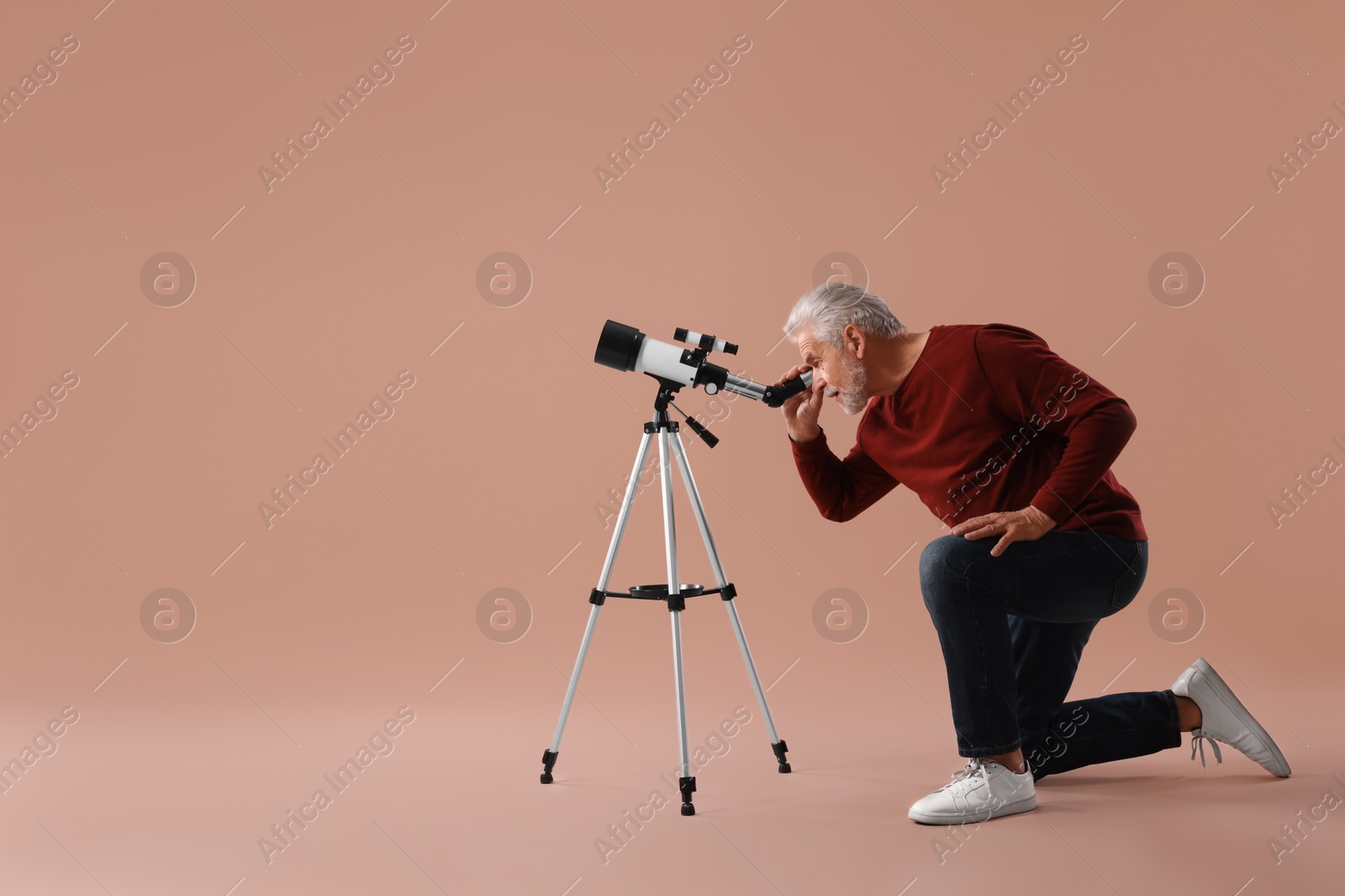 Photo of Senior astronomer looking at stars through telescope on brown background. Space for text