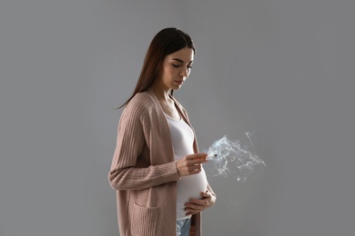 Photo of Young pregnant woman smoking cigarette on grey background