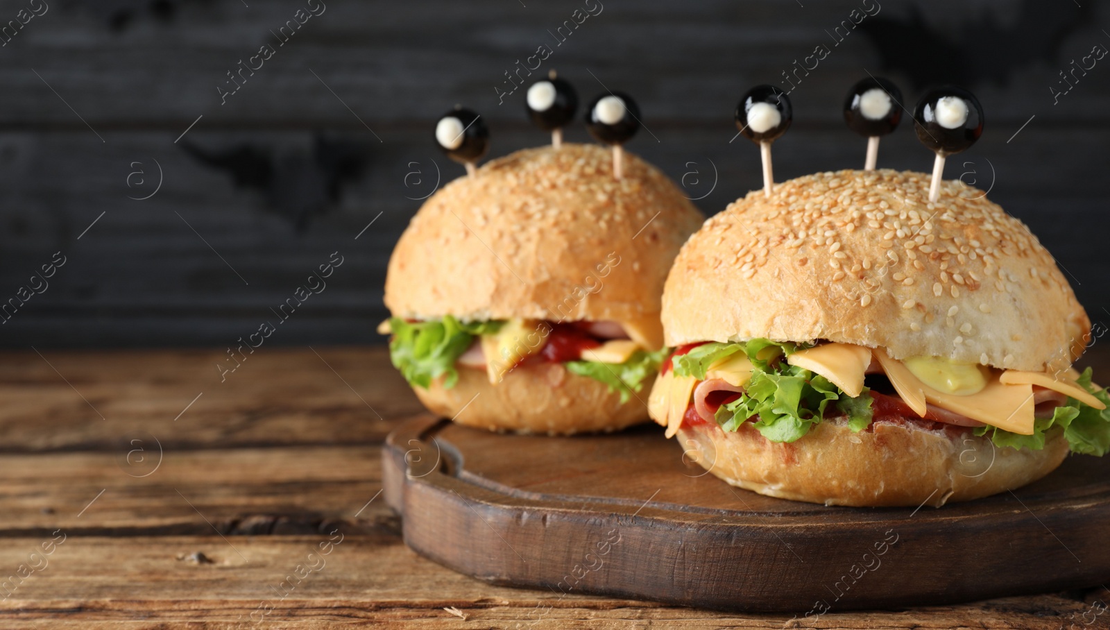 Photo of Cute monster burgers served on wooden table, space for text. Halloween party food