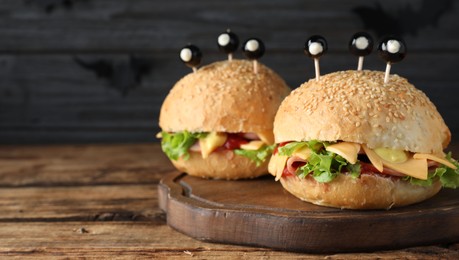Photo of Cute monster burgers served on wooden table, space for text. Halloween party food