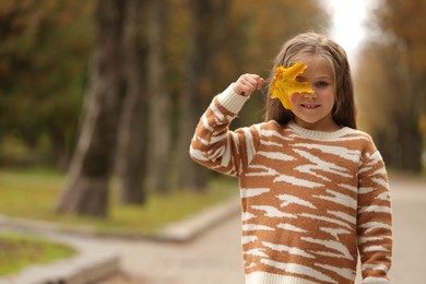 Photo of Portrait of happy girl covering face with autumn dry leaf outdoors, space for text