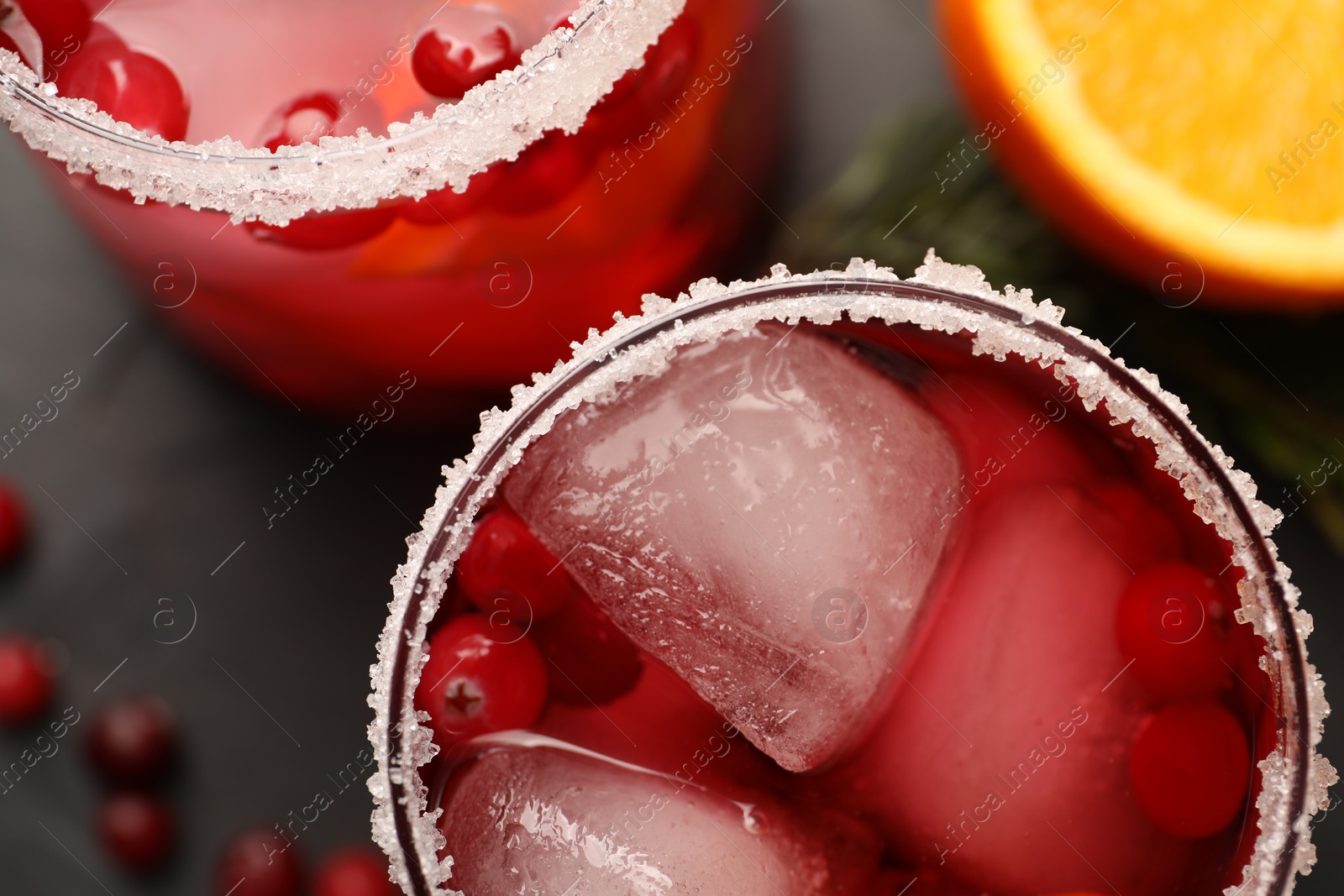 Photo of Tasty cranberry cocktail with ice cubes in glasses on dark gray table, flat lay