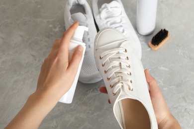 Photo of Woman cleaning stylish footwear on grey marble background, closeup. Shoe care accessories