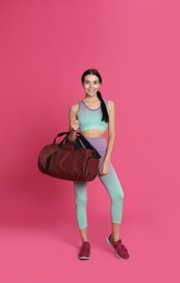 Beautiful woman with sports bag on pink background