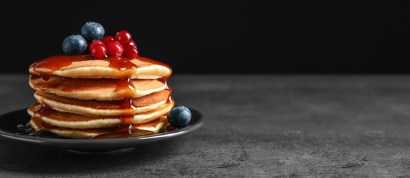 Stack of tasty pancakes with berries and syrup on table, space for text. Banner design