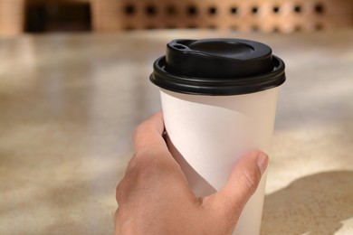 Photo of Woman holding takeaway coffee cup at beige table in cafe, closeup. Space for text