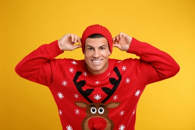 Happy man in Christmas sweater and hat on yellow background