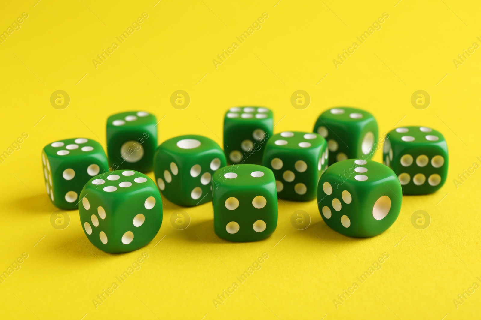Photo of Many green game dices on yellow background, closeup