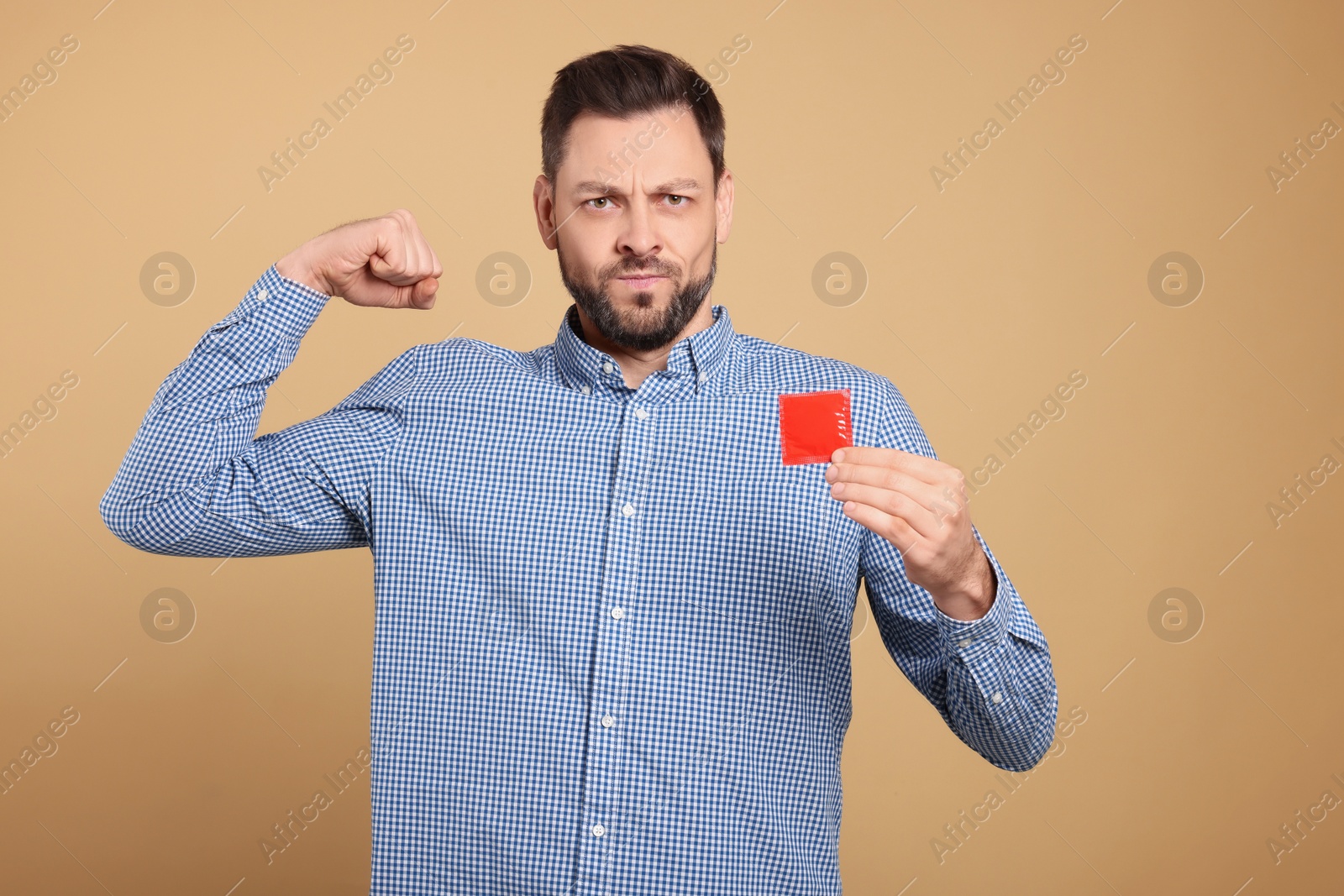 Photo of Handsome man holding condom on beige background