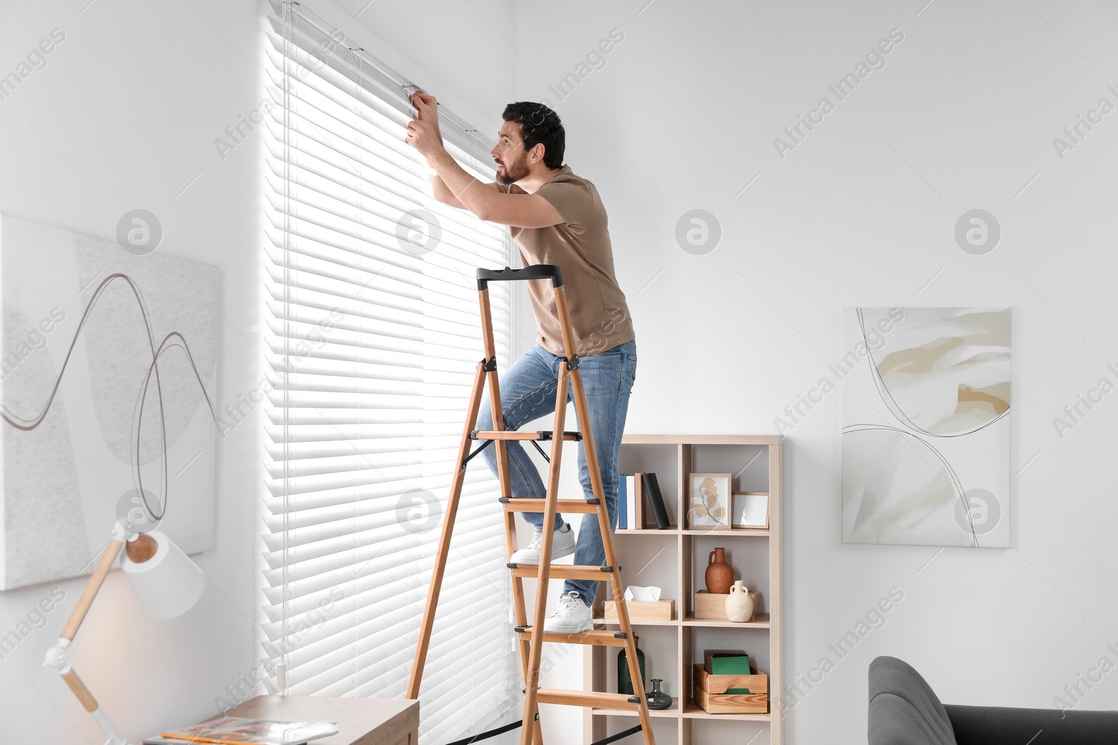 Photo of Man on wooden folding ladder installing blinds at home