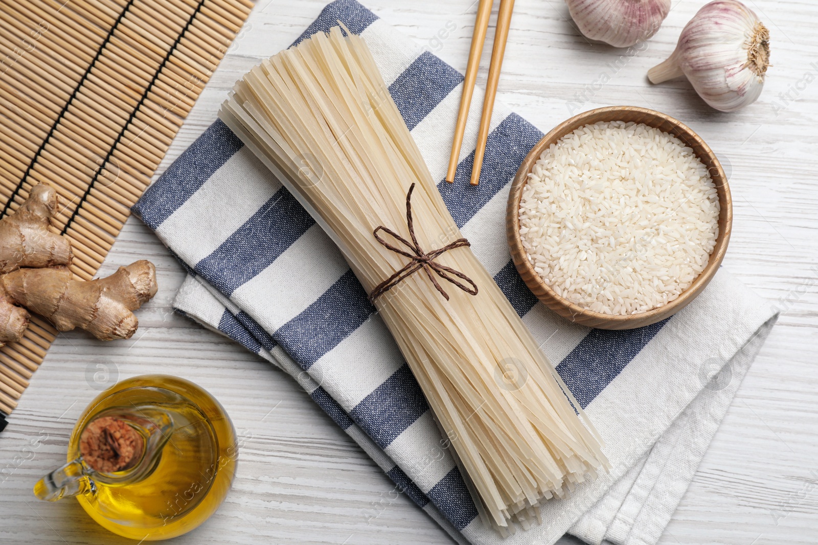 Photo of Bowl with dried rice noodles and ingredients on white wooden table, flat lay
