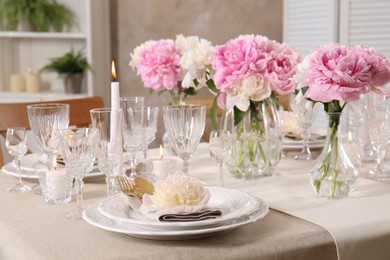 Stylish table setting with beautiful peonies and burning candles indoors