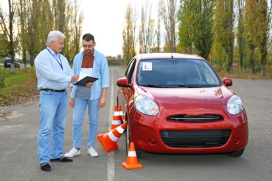 Photo of Senior instructor and man near car outdoors. Passing driving license exam