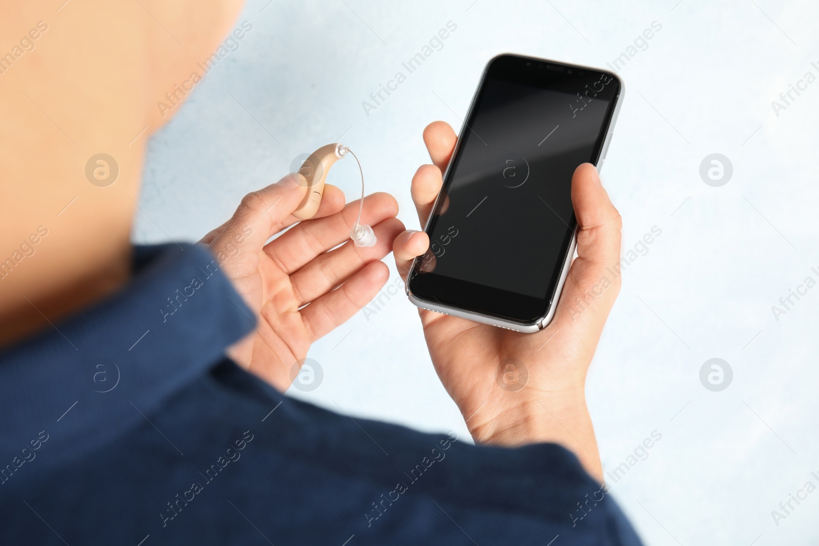 Photo of Patient with hearing aid and smartphone on light background, closeup. Space for text