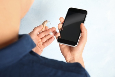 Patient with hearing aid and smartphone on light background, closeup. Space for text