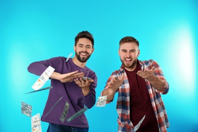 Happy young men throwing money on color background