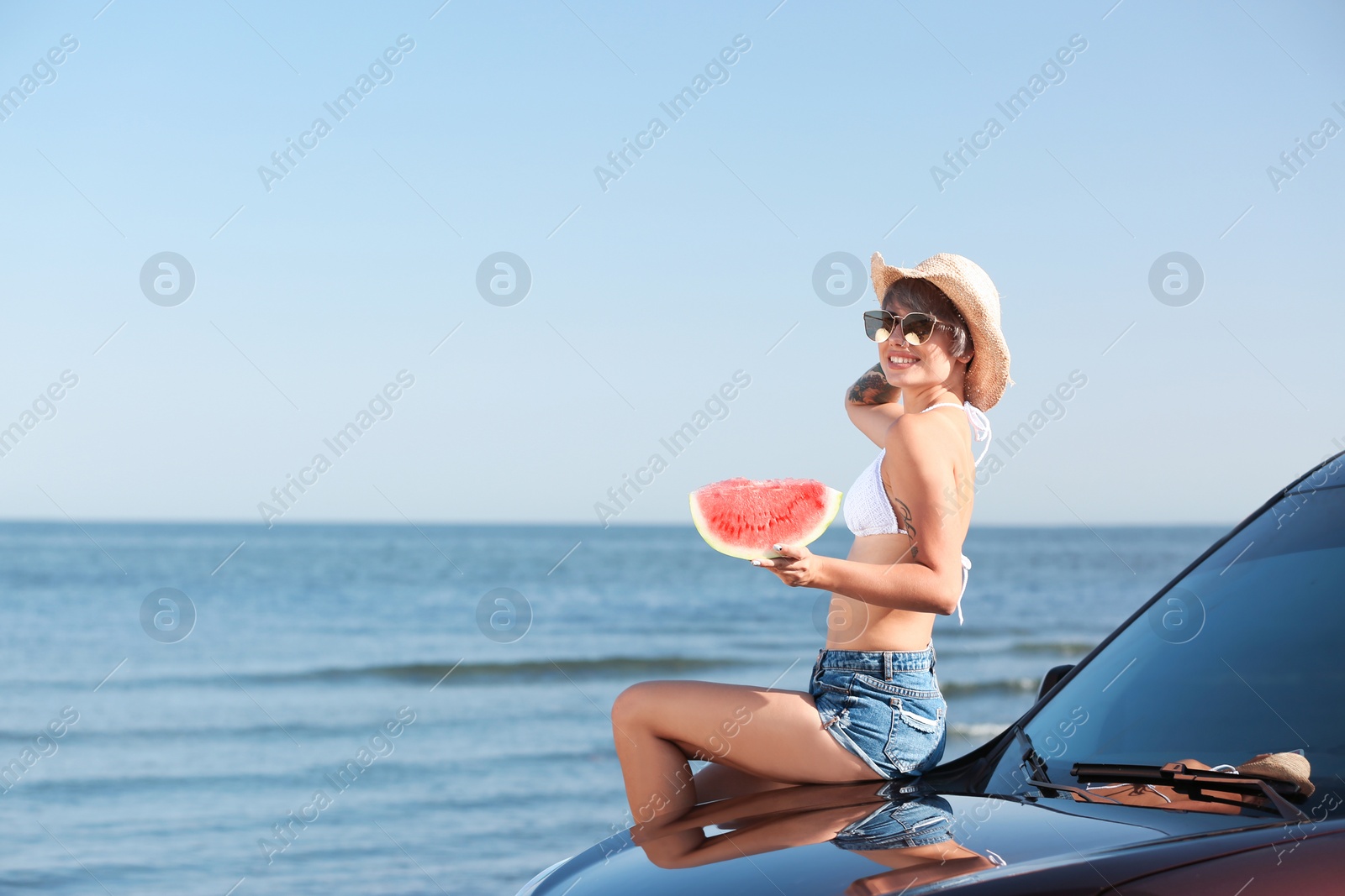 Photo of Young woman with watermelon slice near car on beach. Space for text