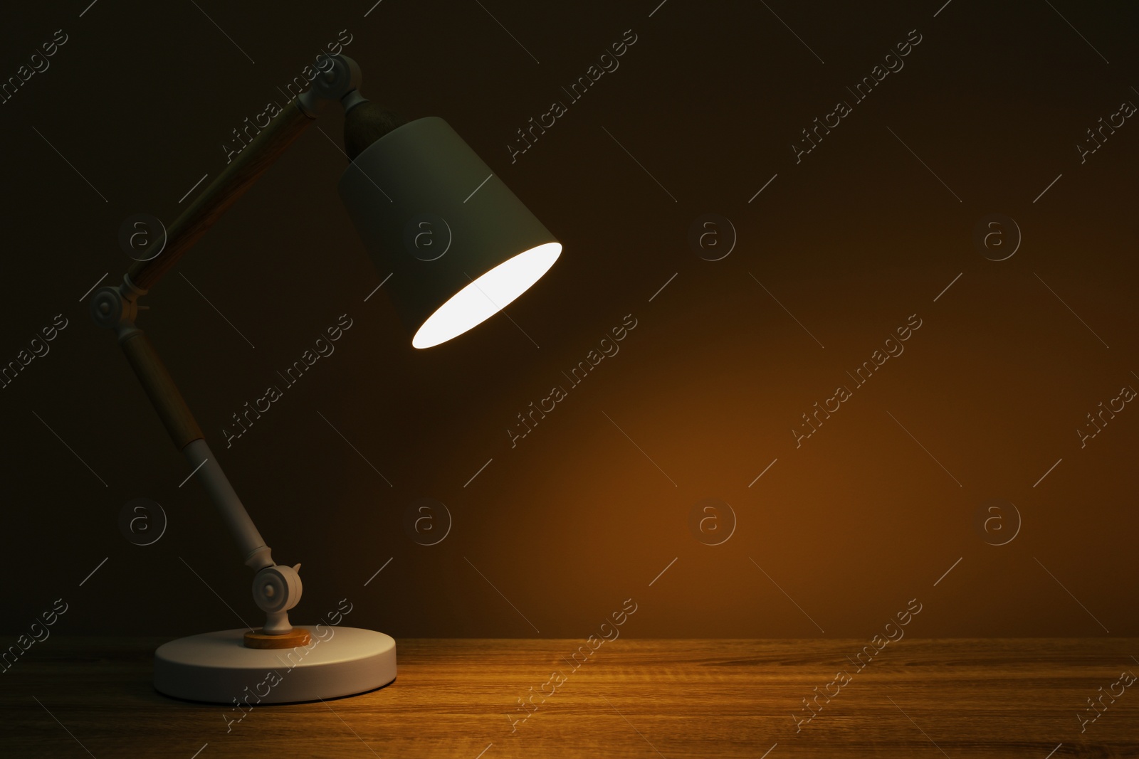 Photo of Stylish modern desk lamp on wooden table at night, space for text