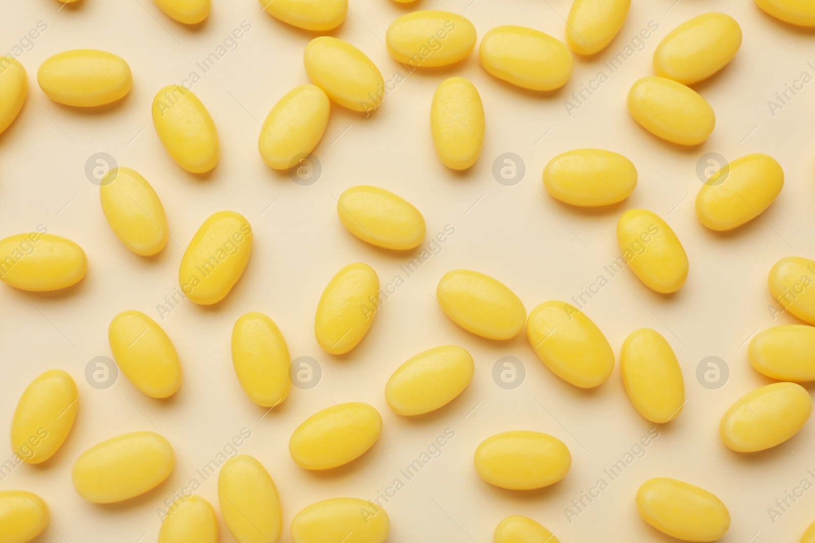 Photo of Many tasty dragee candies on yellow background, flat lay
