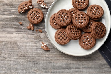 Tasty chocolate sandwich cookies with cream on wooden table, flat lay. Space for text