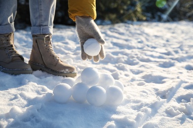 Photo of Woman rolling snowballs outdoors on winter day, closeup