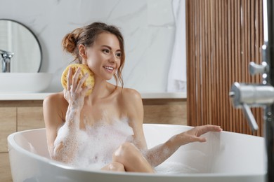 Photo of Beautiful woman with sponge taking bath indoors
