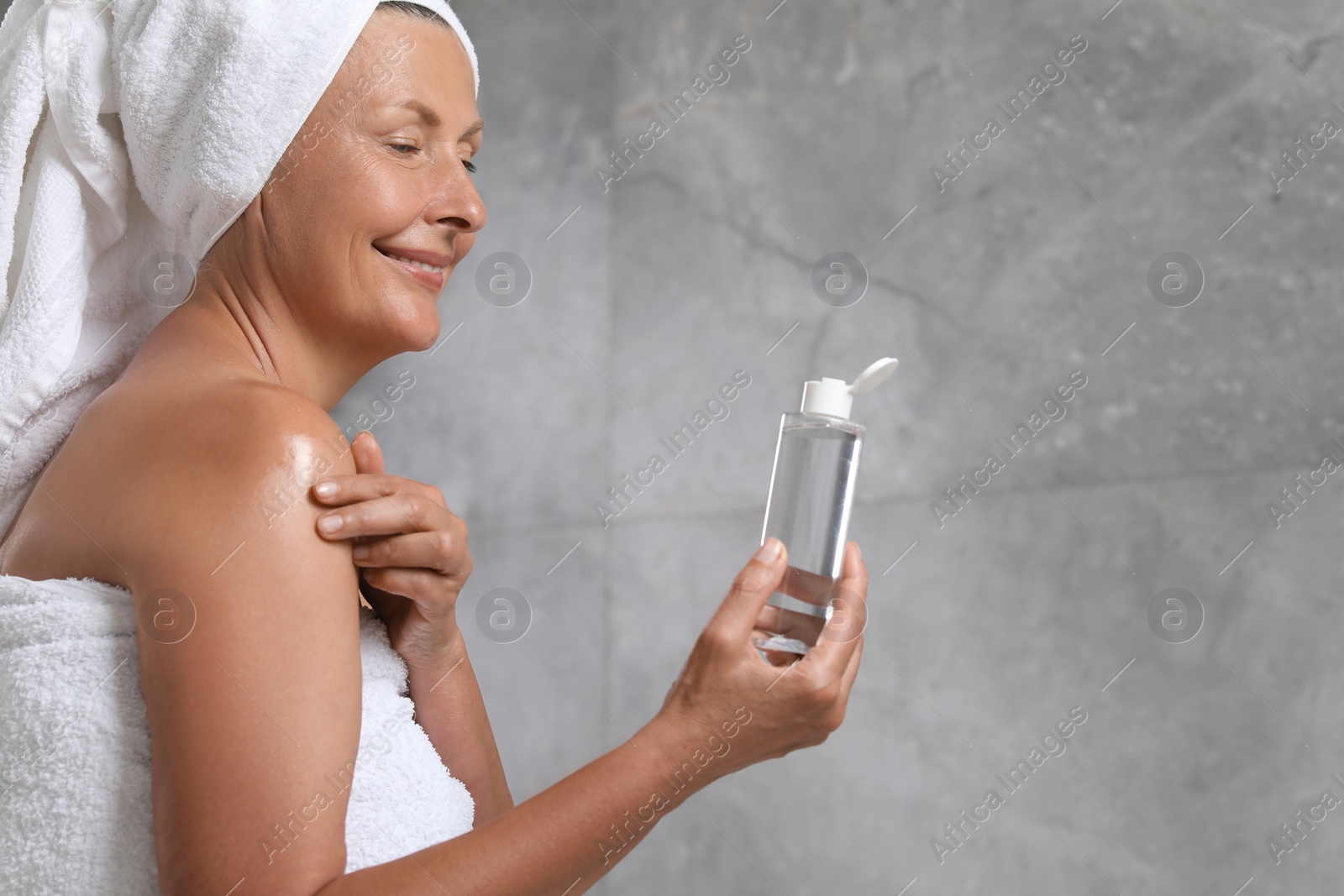 Photo of Happy woman applying body oil onto shoulder near grey wall