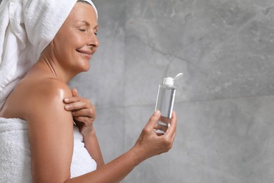 Photo of Happy woman applying body oil onto shoulder near grey wall