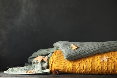 Different soft plaids, dry leaves and fir cone on black wooden table. Space for text