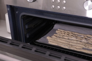 Photo of Baking tasty homemade breadsticks with spices in kitchen oven. Cooking traditional grissini