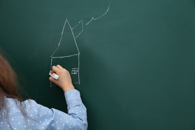 Little child drawing house on chalkboard, closeup. Space for text