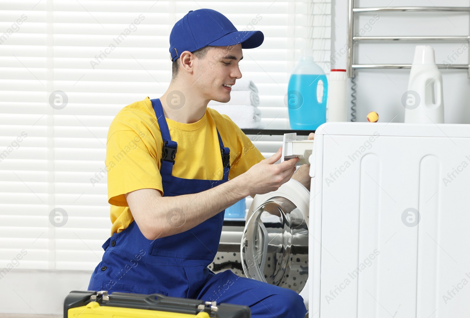 Photo of Smiling plumber repairing washing machine in bathroom