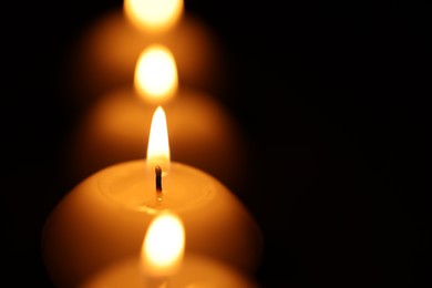 Photo of Burning wax candles on black background, closeup. Space for text