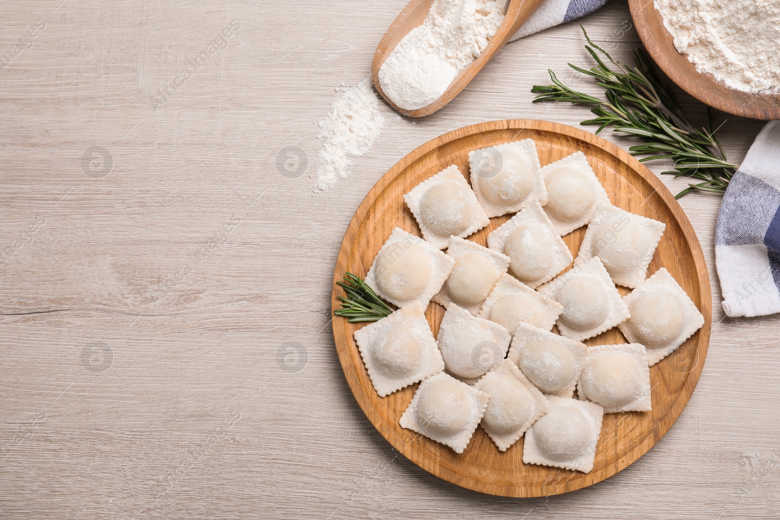 Photo of Uncooked ravioli and rosemary on white wooden table, flat lay. Space for text