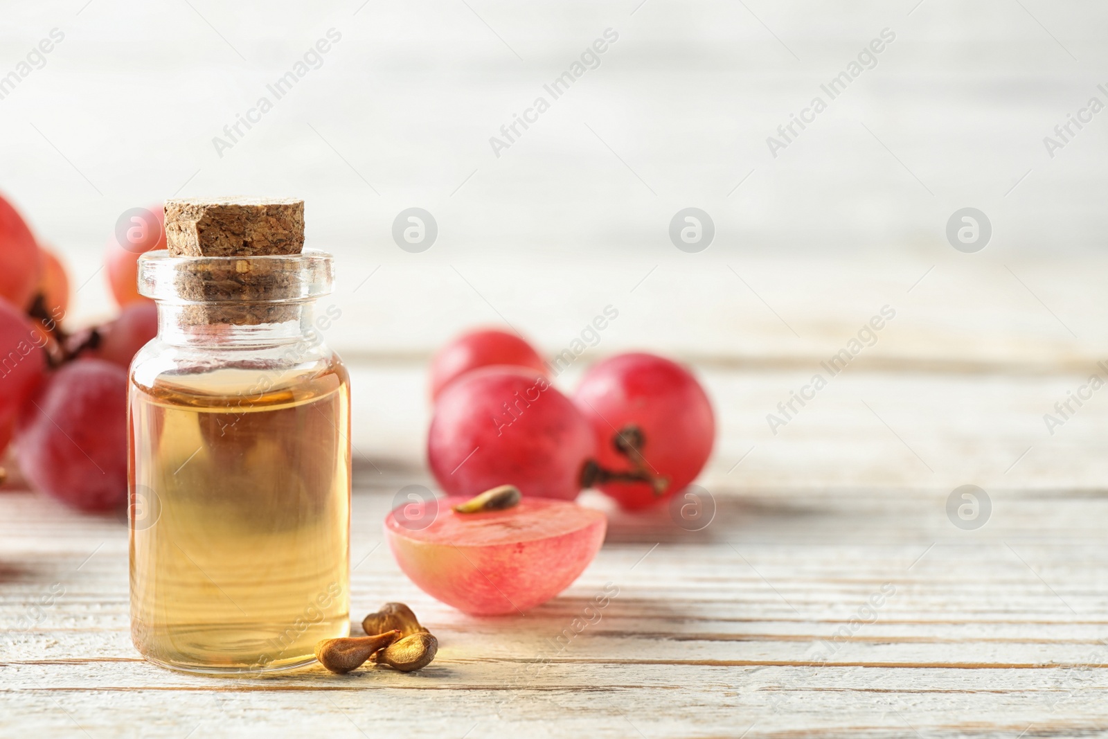 Photo of Organic red grapes, seeds and bottle of natural essential oil on white wooden table. Space for text