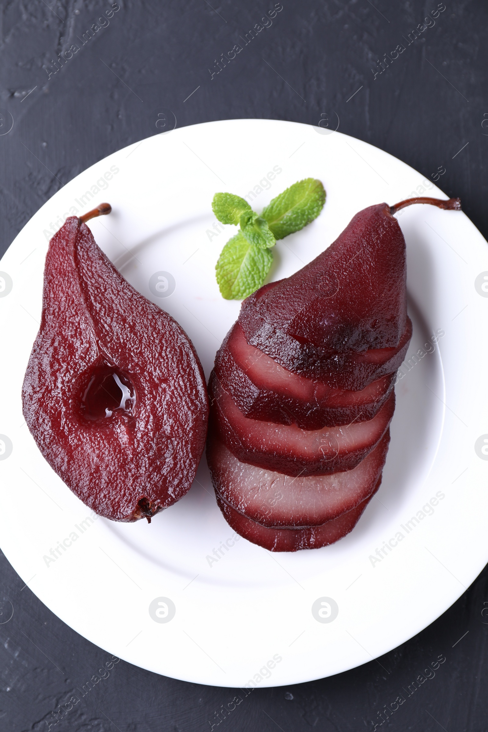 Photo of Tasty red wine poached pears and mint on black table, top view