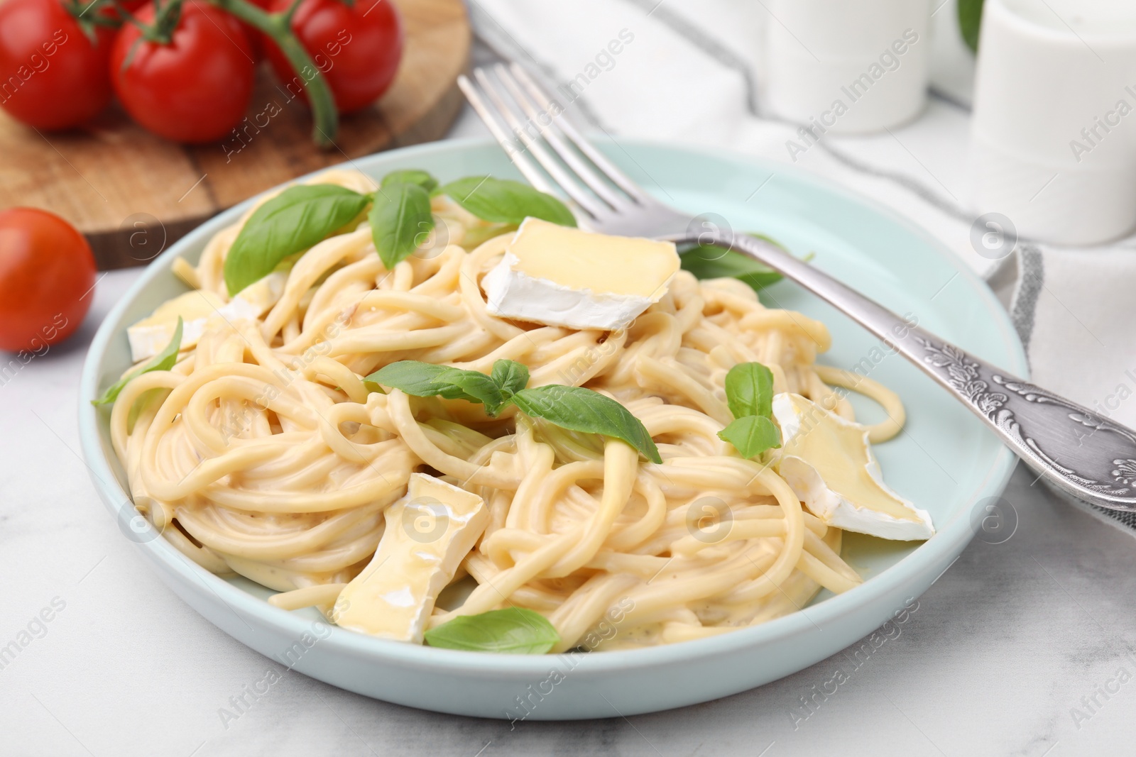 Photo of Delicious pasta with brie cheese, basil and fork on white marble table, closeup