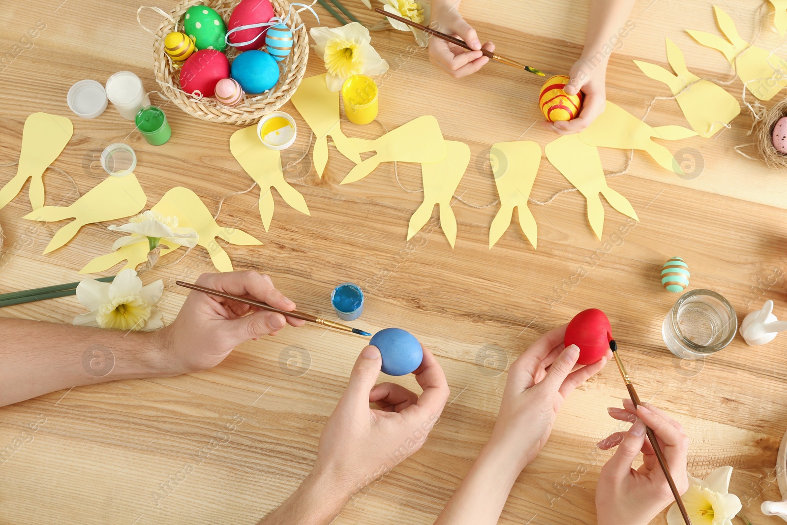 Photo of Father, mother and their child painting Easter eggs at wooden table, above view