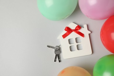 Photo of House model with red bow, keys and colorful balloons on light background, flat lay. Housewarming party