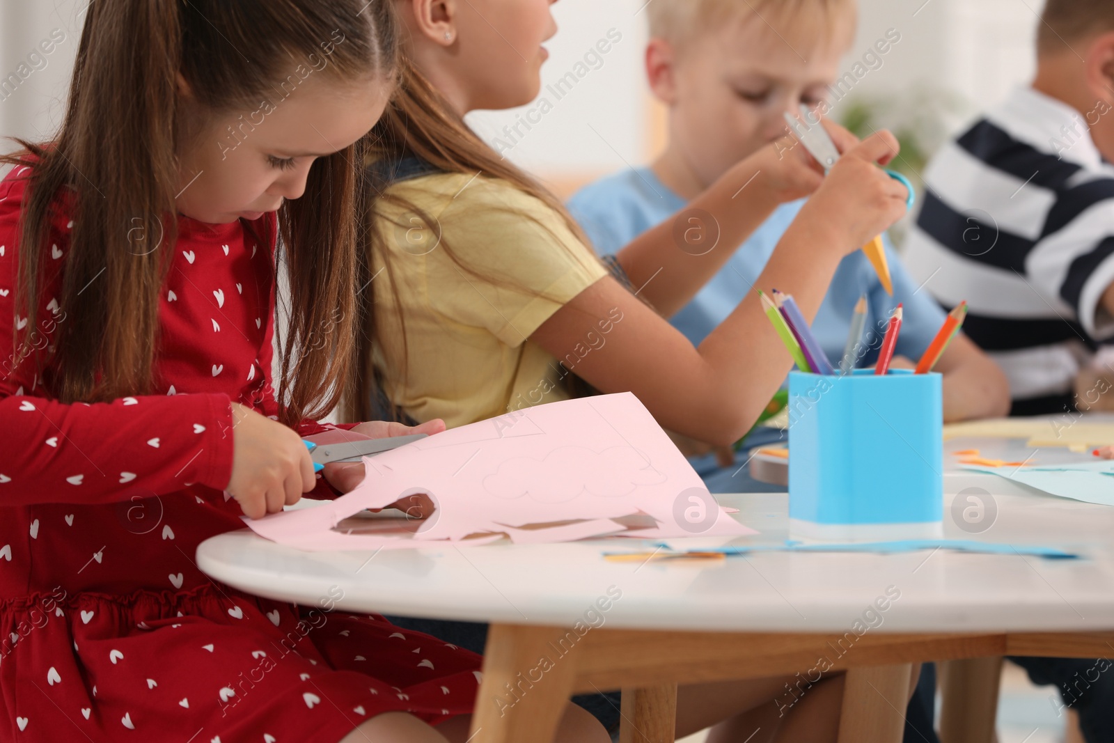 Photo of Group of cute little children making toys from color paper at desk in kindergarten. Playtime activities