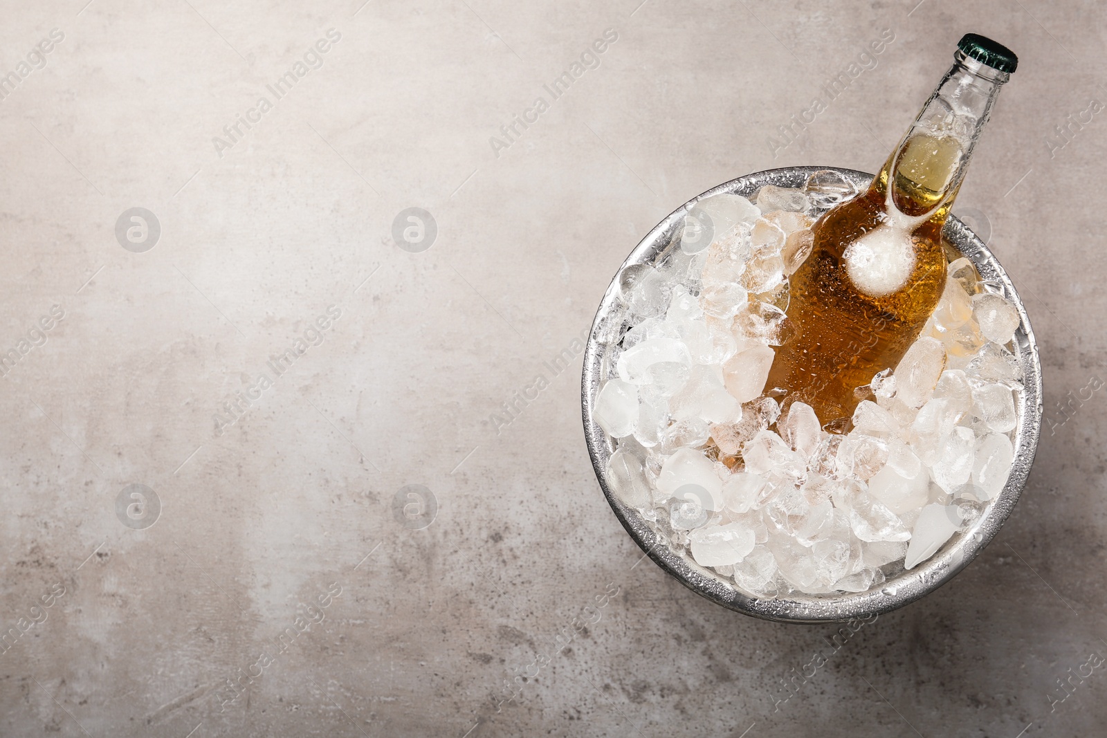 Photo of Beer in metal bucket with ice on grey table, top view. Space for text