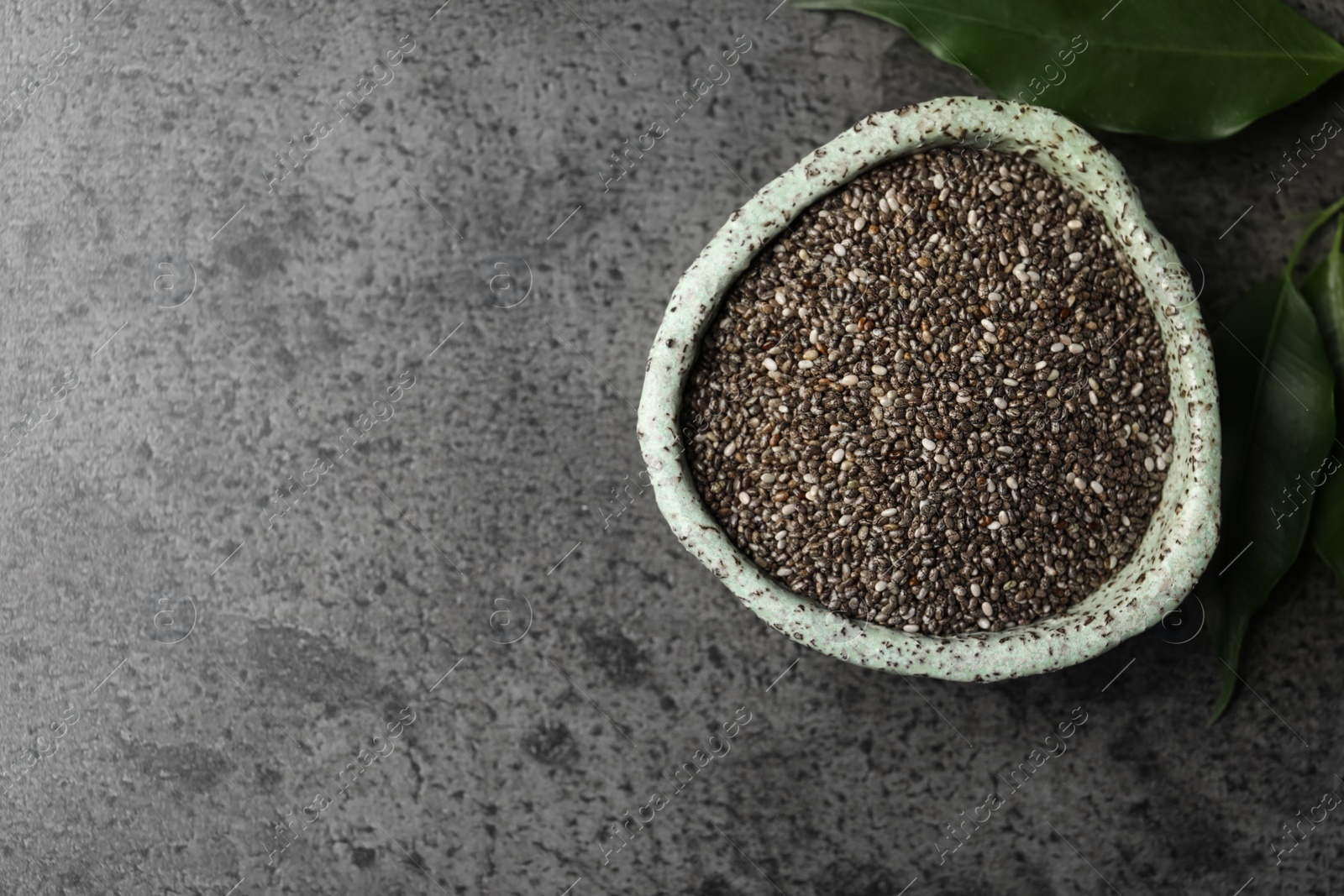 Photo of Bowl with chia seeds and leaves on grey table, flat lay. Space for text