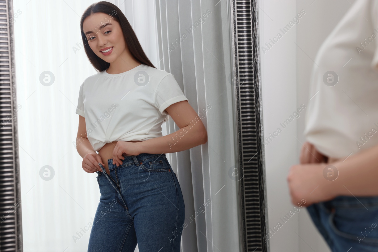 Photo of Young woman in stylish jeans near mirror indoors