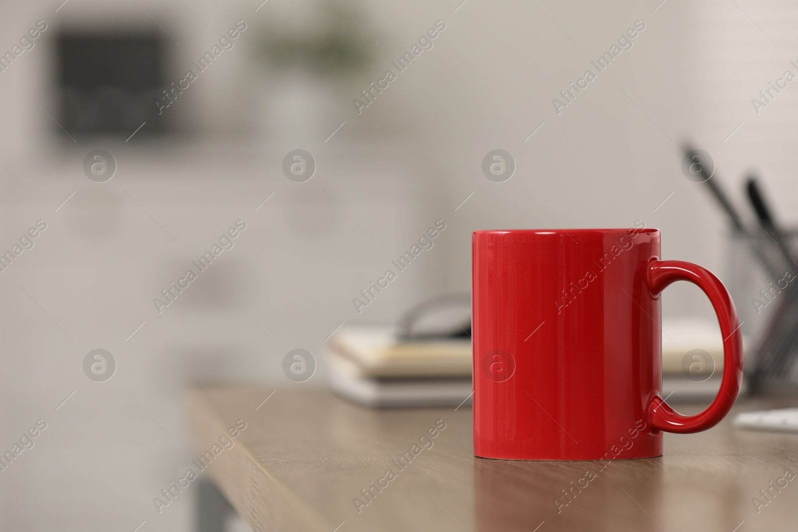 Photo of Red ceramic mug on wooden table at workplace. Space for text