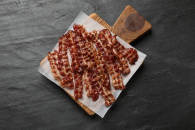 Photo of Slices of tasty fried bacon on black table, top view