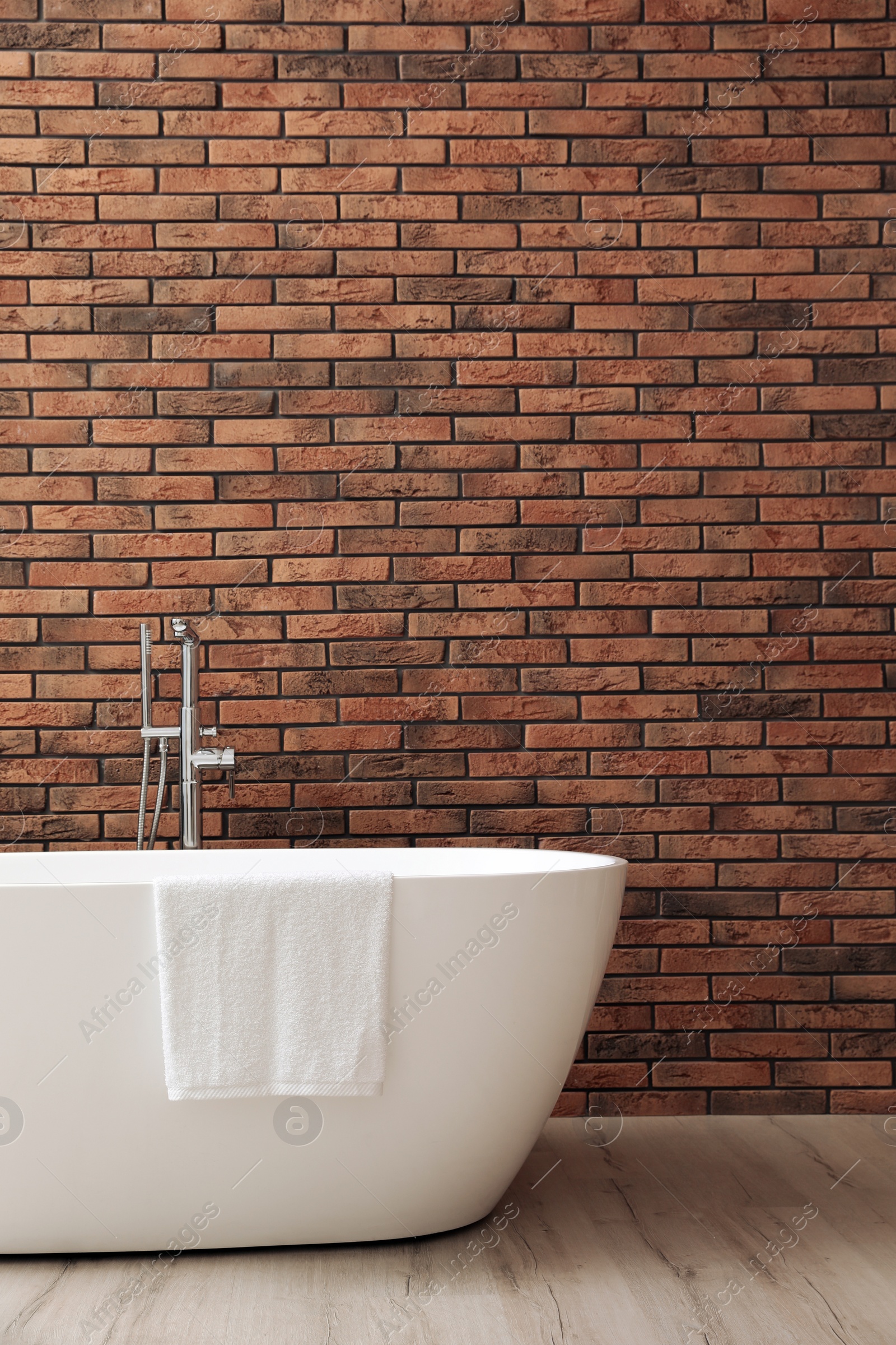 Photo of Modern ceramic bathtub with towel near brick wall