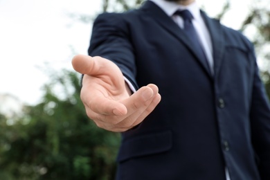 Photo of Businessman giving helping hand on blurred background outdoors