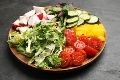 Photo of Vegetarian diet. Plate with tasty vegetables on black table, closeup