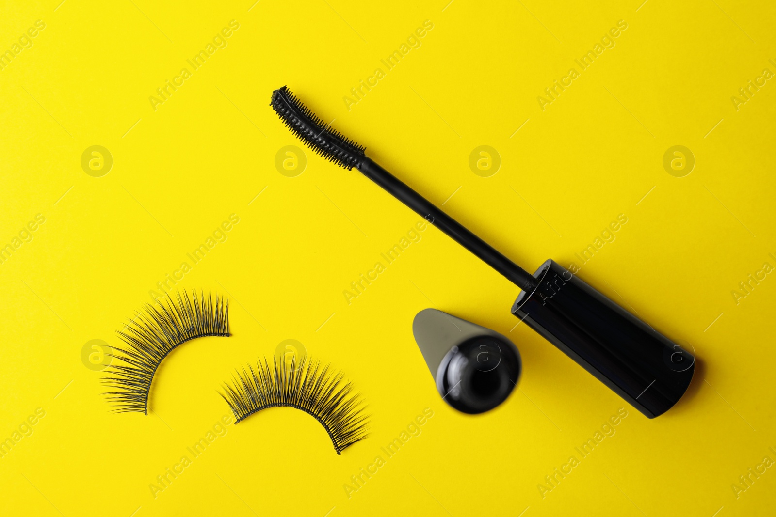 Photo of Black mascara and fake eyelashes on yellow background, flat lay. Makeup product