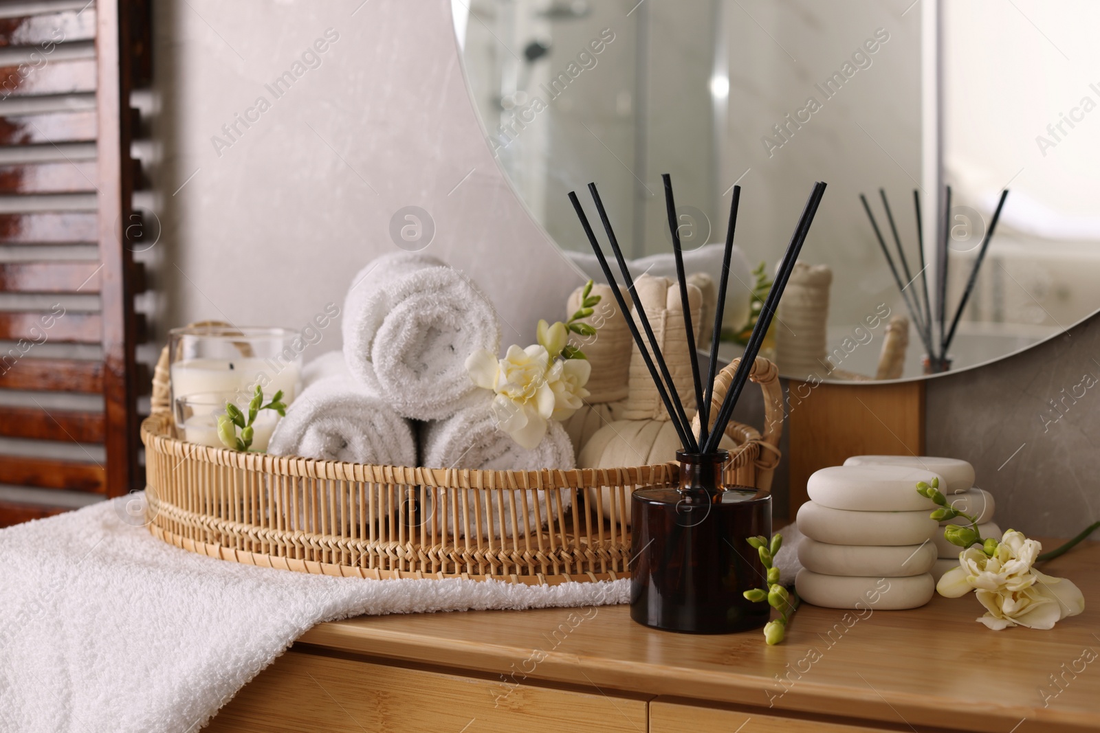 Photo of Aromatic reed air freshener, rolled towels and spa stones on wooden table indoors